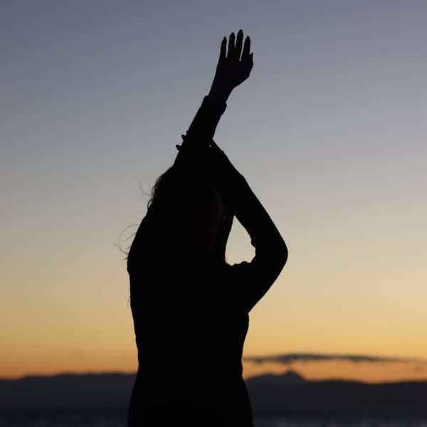 Person stretching peacefully outdoors during a beautiful sunset.